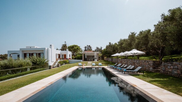 Une piscine entourée d’un mur de pierre et de verdure, avec des chaises longues et des parasols.