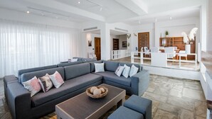 Un vaste espace de vie comprenant un grand canapé d’angle, une table basse et un coin repas avec une table et des chaises blanches.