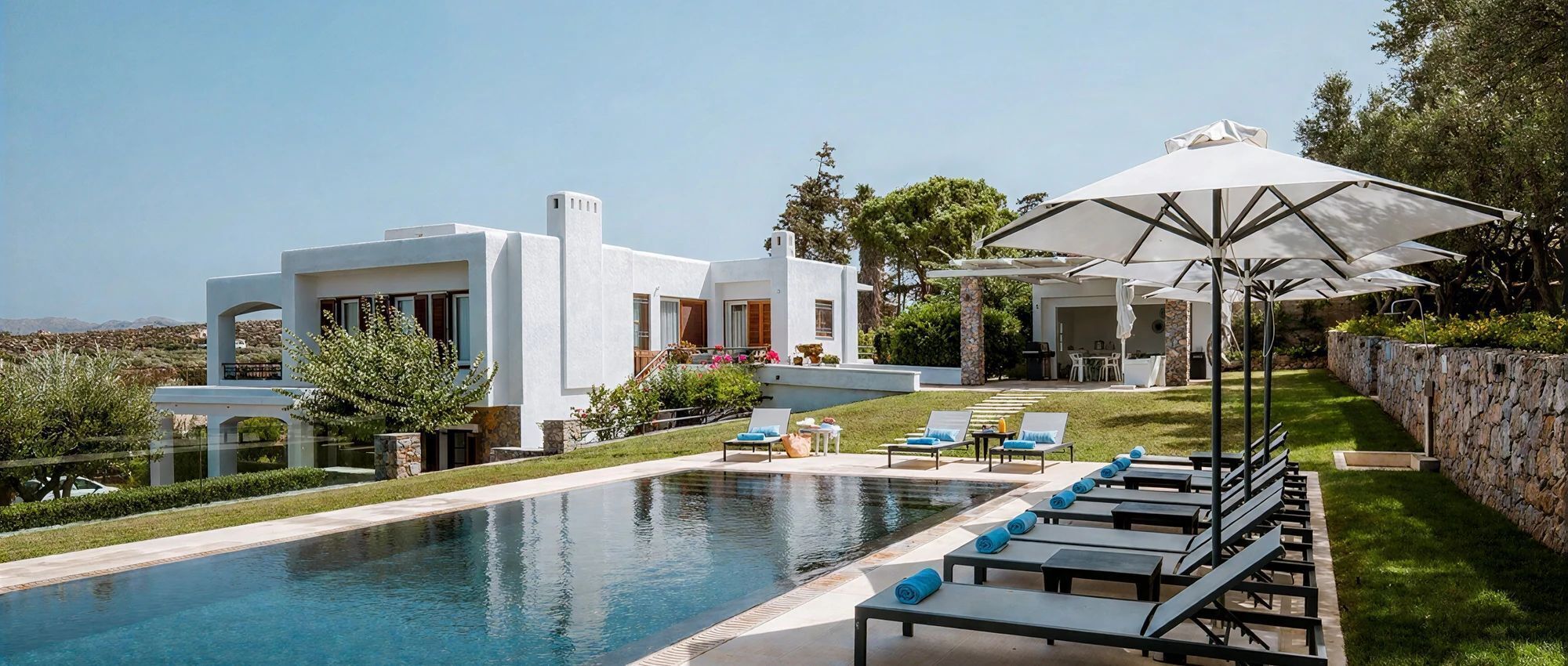 Une maison moderne dotée d’une piscine, d’un espace salon extérieur et d’un mur en pierre.