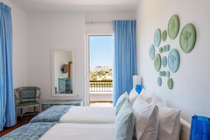 A room with two beds, a chair, a mirror, and a view of the mountains through a balcony.