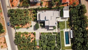Vue aérienne d’une maison moderne dotée d’une piscine, entourée de jardins bien entretenus et d’une allée pavée.