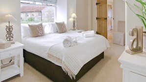 A bedroom with a large bed, two bedside tables, a window with a view, and a wooden door.