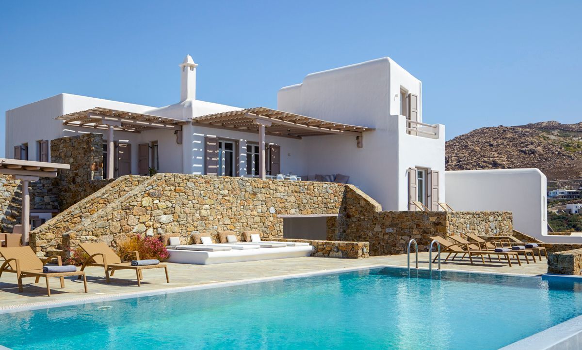 A modern white building with a stone facade, a swimming pool, and lounge chairs.