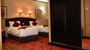 Habitación de hotel con dos camas, alfombra roja estampada, luces fijadas a la pared y obras de arte.