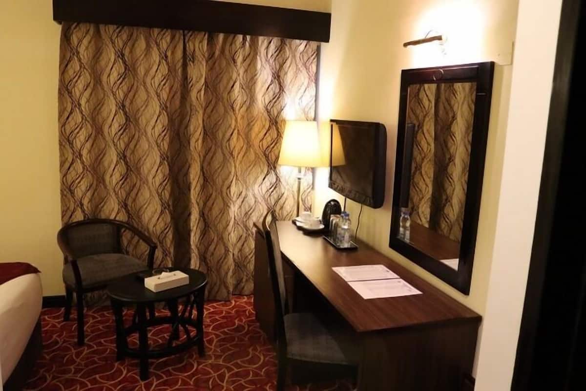 Ein Hotelzimmer mit strukturiertem Wandteppich, einem Schreibtisch mit Lampe, einem Sessel und einem Bett.