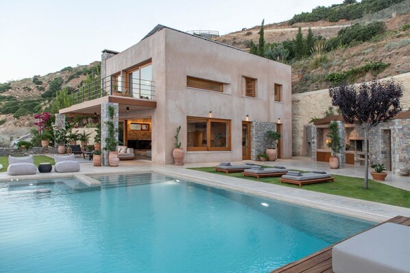 Una casa moderna de dos pisos amb piscina, mobiliari exterior i un mur de pedra.