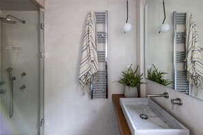 Un bany amb un espai de dutxa de vidre, un lavabo amb taulell de marbre i tovalloles penjades en un suport.