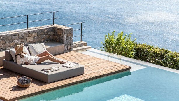 Un espace aménagé au bord de la piscine, avec un mur en pierre, une terrasse en bois et un fauteuil de relaxation.