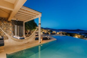 Ein Pool ohne Rand mit Blick auf das Meer und die Berge, eine Hängematte und Sitzgelegenheiten im Freien.