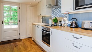 A modern kitchen with white cabinetry, a stainless steel range hood, a built-in oven, a microwave, and a wooden countertop.