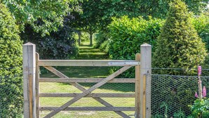 A wooden gate with a metal mesh fence, surrounded by lush greenery and a pathway.