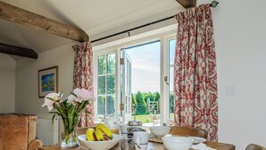 A dining area with a wooden table, chairs, a vase with flowers, and a view of greenery outside.