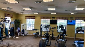 A gym with various exercise equipment, large windows, and a television screen.