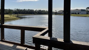 A wooden deck overlooking a calm river with a clear sky and distant buildings.