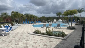 A poolside area with lounge chairs, a swimming pool, palm trees, and a cloudy sky.