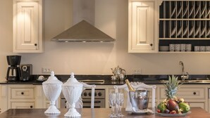 Une cuisine avec des armoires blanches, une hotte de cuisinière en acier inoxydable, un meuble à vin et un panier de fruits posé sur le comptoir.