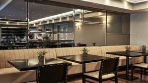 Un espace repas moderne comprenant un canapé, des tables et des chaises. Une grande fenêtre offre une vue sur la cuisine et le bar.