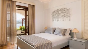 A bedroom with a bed, two bedside tables, a window with curtains, a wall-mounted plant, and a view of the outdoors. - Villa Tersanas - Four Bedroom Villa, Sleeps 9 (Livadi)