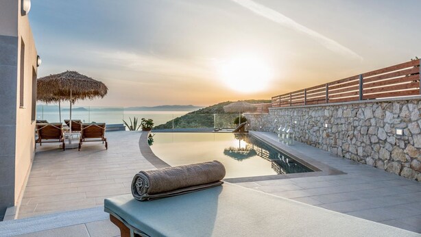 A sunlit infinity pool with a stone wall and wooden railing, overlooking a scenic view. - Villa Tersanas - Four Bedroom Villa, Sleeps 9 (Livadi)