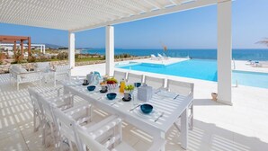 A covered outdoor dining area with white furniture, a pool, and a view of the sea.
