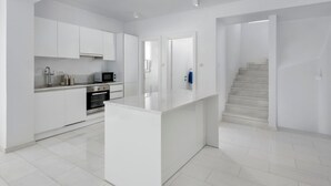 A modern kitchen with white cabinetry, a central island, and a staircase leading to another level.