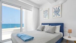 A modern bedroom with a large bed, a view of the sea, and two framed artworks on the wall.