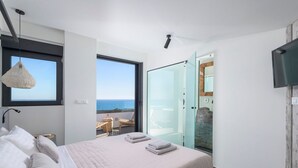 Une chambre moderne avec un grand lit, une vue sur la mer et une porte vitrée donnant sur un balcon.