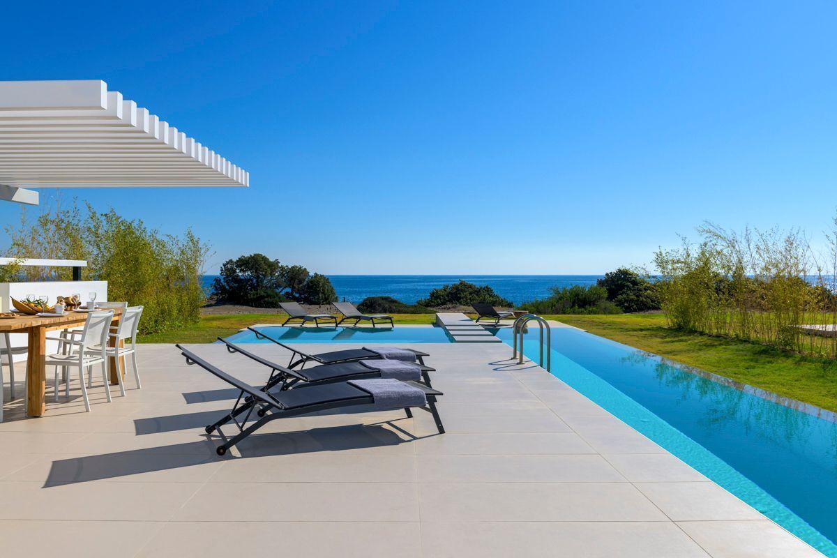 A poolside area with lounge chairs, a table, and a pergola overlooking the ocean.
