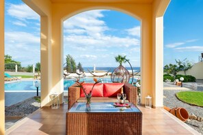 Un espace aménagé au bord de la piscine, avec une table en osier, des coussins rouges et une bouteille de champagne.