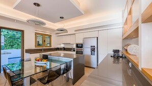 A modern kitchen with a glass dining table, stainless steel appliances, and a view of greenery outside. - Villa Sappho - Four Bedroom Villa, Sleeps 8 (Ialysos)