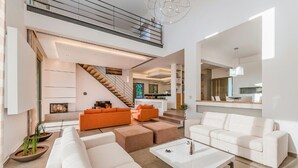 A spacious living area with a staircase, a fireplace, and a kitchen in the background. - Villa Sappho - Four Bedroom Villa, Sleeps 8 (Ialysos)