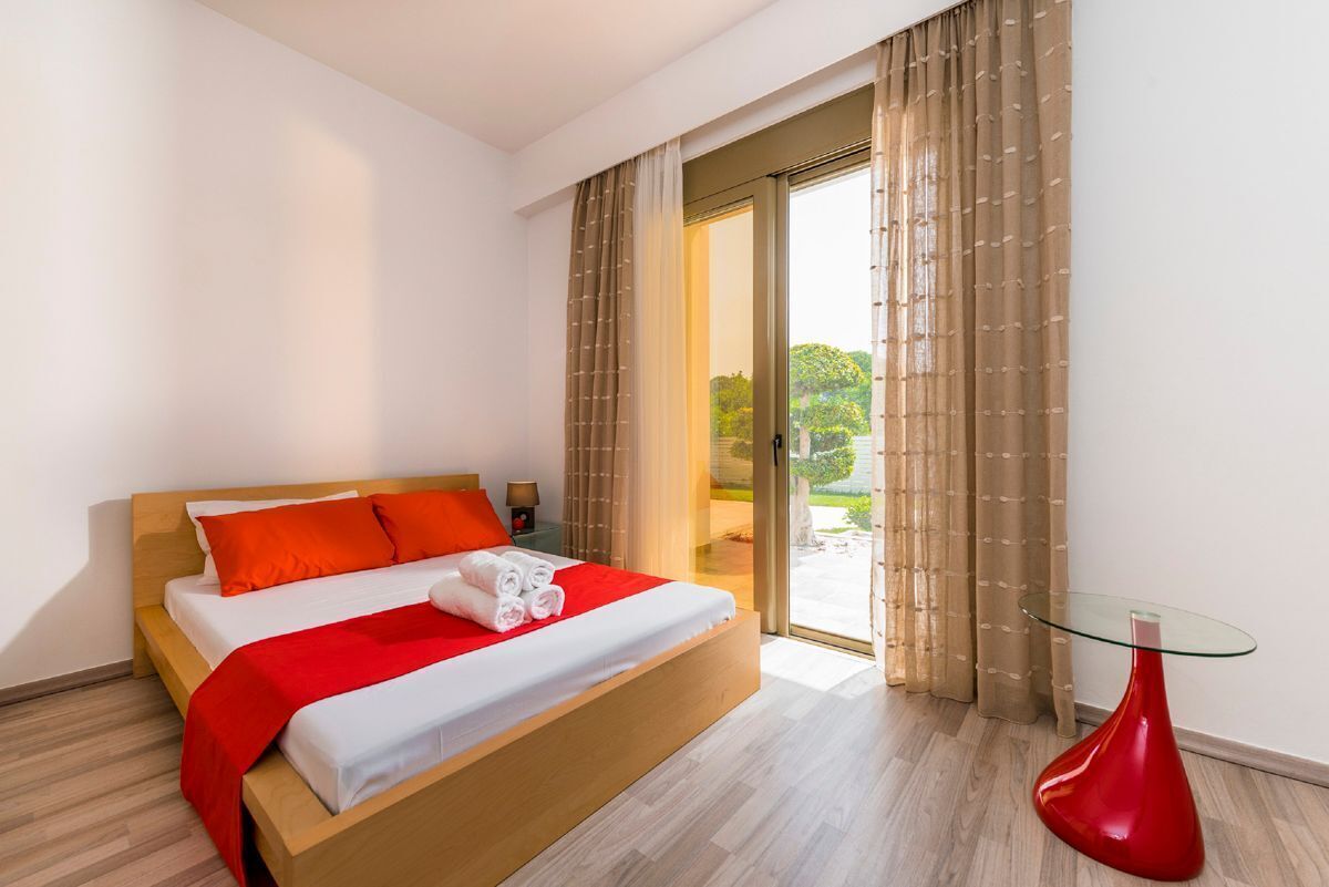 A modern hotel room with a wooden bed, red bedding, and a glass table.