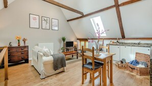A loft-style room with a dining area, a sofa, a TV, and a kitchen with a window.