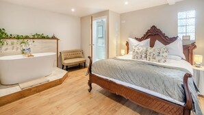 A bedroom with a large bed, a wooden headboard, a vanity with a mirror, a bench, and a window.