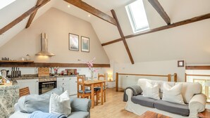 A loft-style room with exposed wooden beams, a dining area, a sofa, and a wooden coffee table.