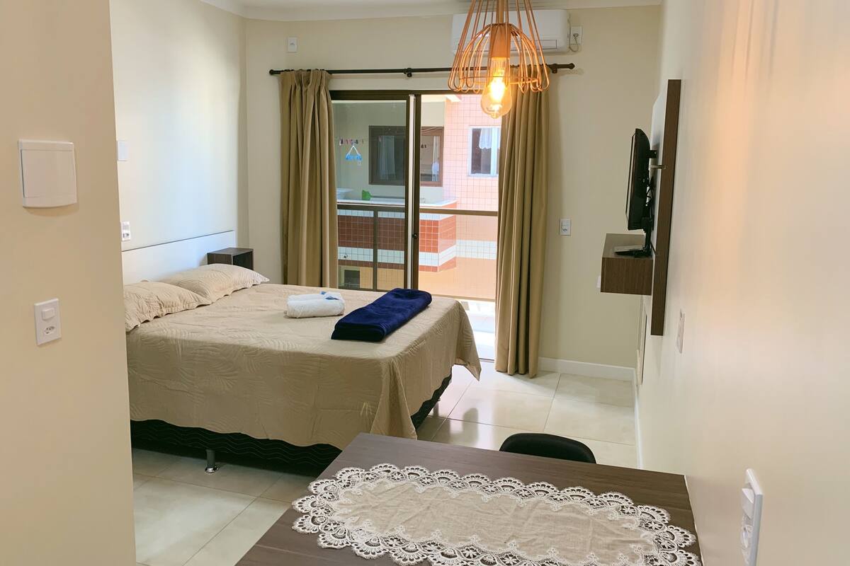 Une chambre d’hôtel avec un lit, une table recouverte d’une nappe en dentelle, un luminaire suspendu et une vue sur le balcon extérieur.