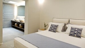 A modern bedroom with a large bed, bedside tables, and a built-in bathroom with a sink and shelves.