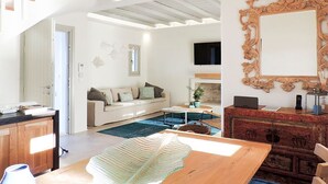 A modern living room with a wooden dining table, a sofa, and a TV mounted on the wall.