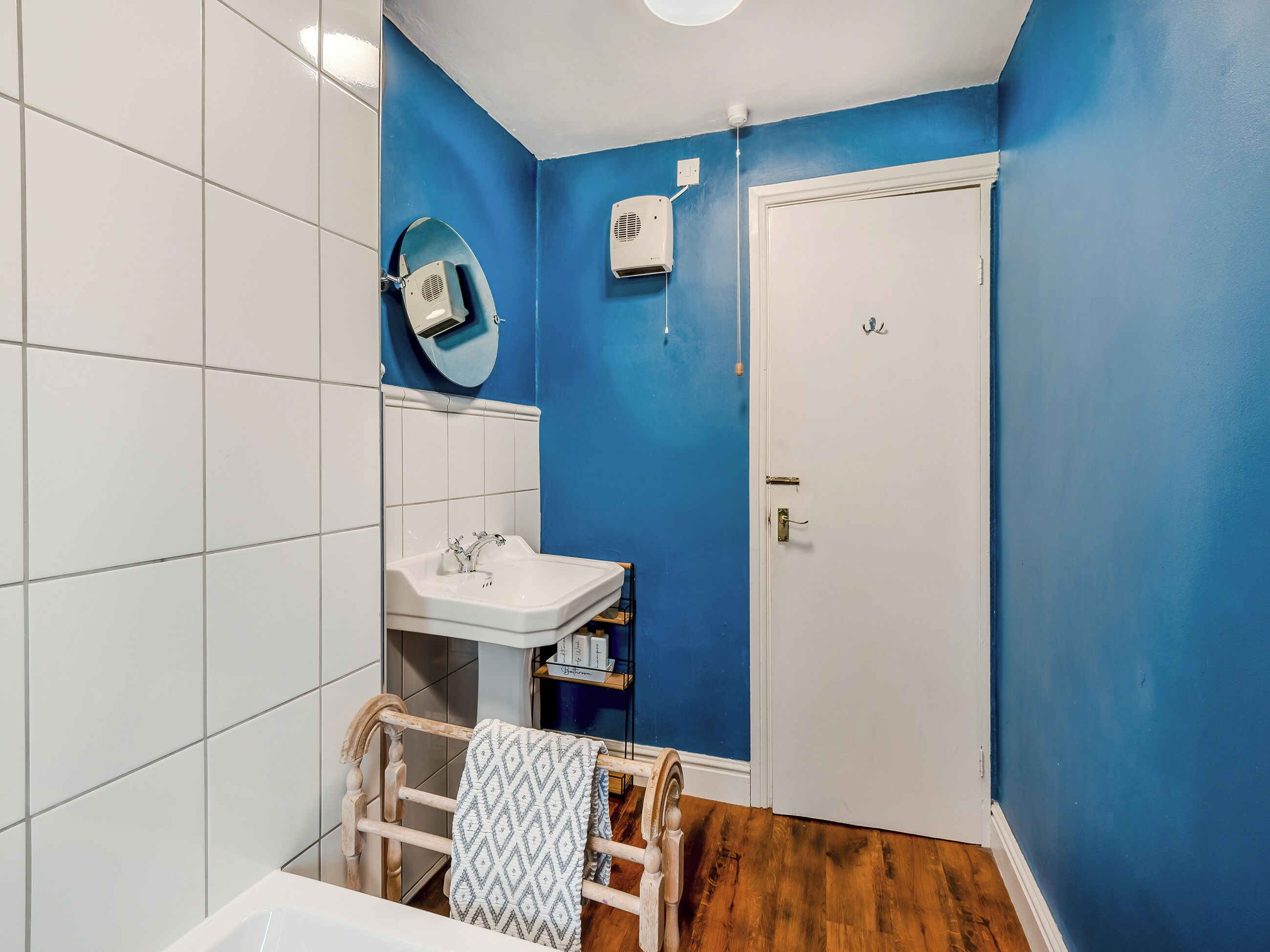 Une salle de bain avec un lavabo blanc, des murs bleus et un plancher en bois.