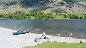 Ein ruhiger See mit einem grünen Boot am Ufer, umgeben von Wiesen und einem Berg im Hintergrund.