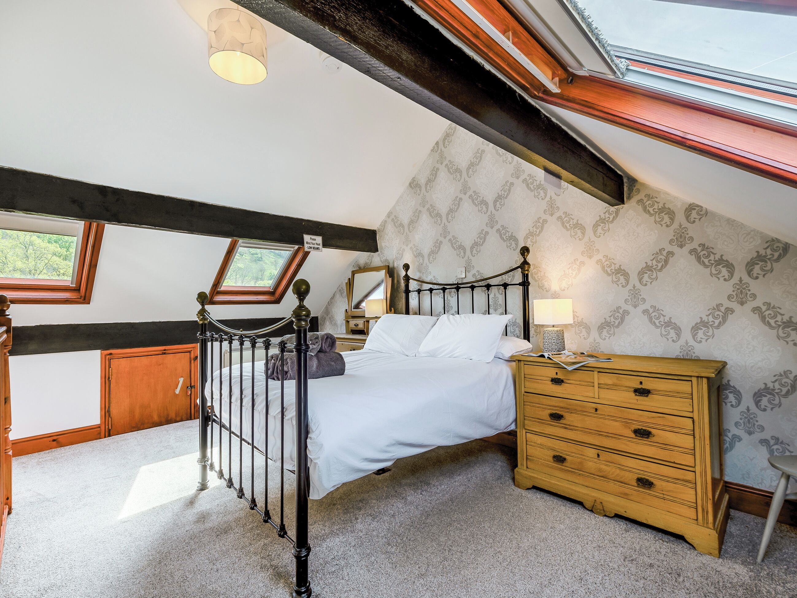 Een slaapkamer met dakraam, een bed, een houten dressoir en een nachtkastje.