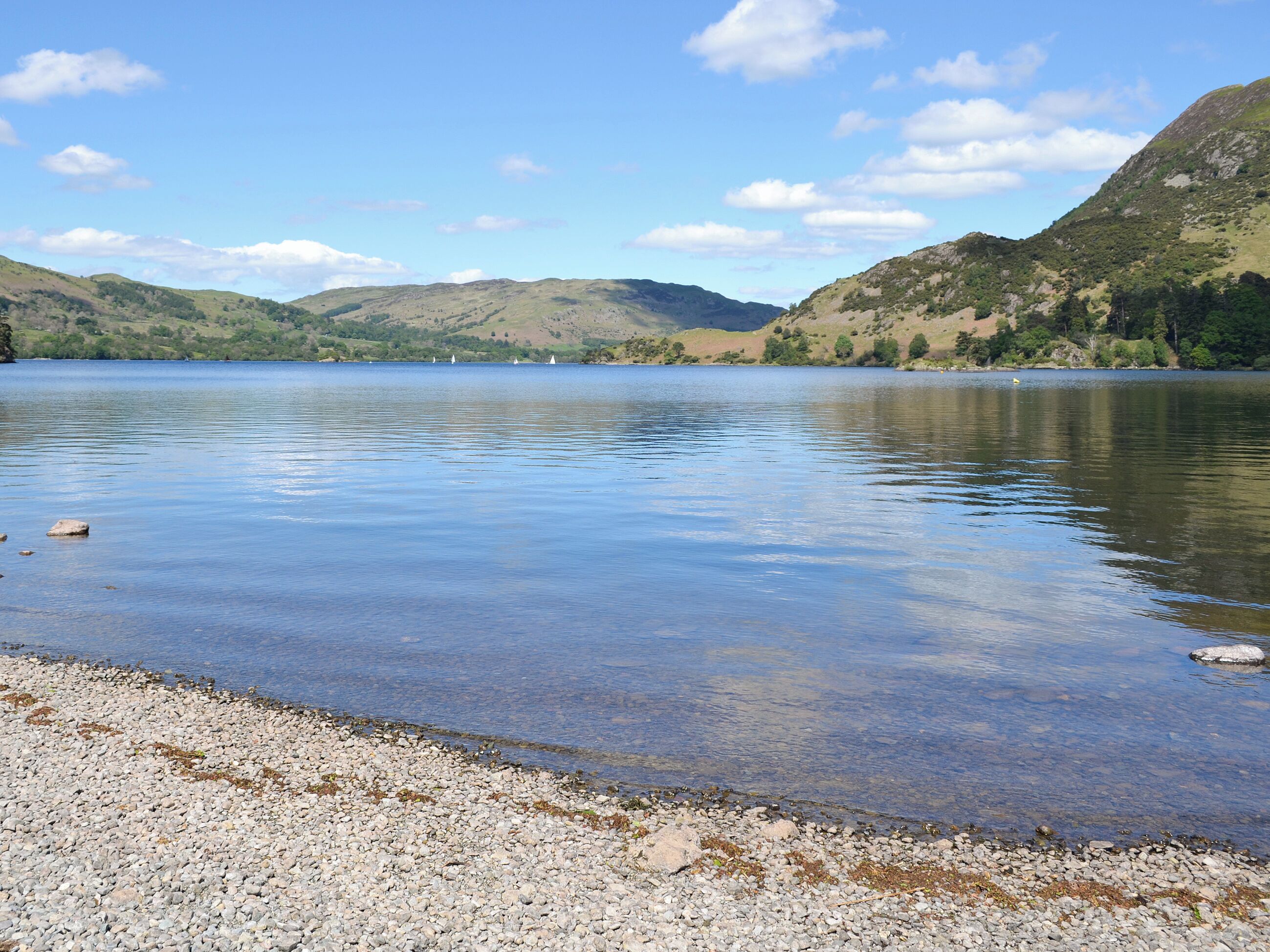 Un lago tranquilo con orilla pedregosa y colinas a lo lejos.
