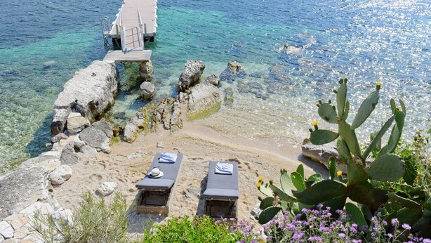 A beach with clear water, a wooden pier, and two sun loungers.