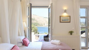 A bedroom with two beds, a view of the sea, and a balcony with a wicker chair.