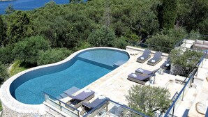 A swimming pool with lounge chairs and a view of the sea.