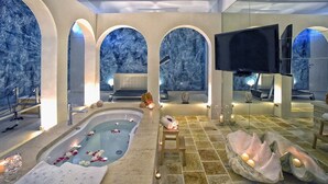A luxurious spa room with a large bathtub, arched alcoves, a television, and candles.