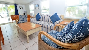 A room with a striped sofa, a wicker chair, a wooden table, and a view of the outside. - FL Keys Cottage with Ocean Views - Venture Out Unit 395 (Cudjoe Key)
