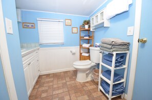 Une salle de bain équipée de toilettes, d’un lavabo et d’étagères où sont rangées les serviettes.