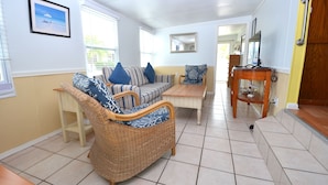 A living room with a wicker sofa, striped armchair, and a wooden coffee table. - FL Keys Cottage with Ocean Views - Venture Out Unit 395 (Cudjoe Key)