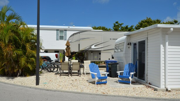 A recreational vehicle (RV) parked in a residential area with a small outdoor seating area, including a table and chairs. - FL Keys Cottage with Ocean Views - Venture Out Unit 395 (Cudjoe Key)